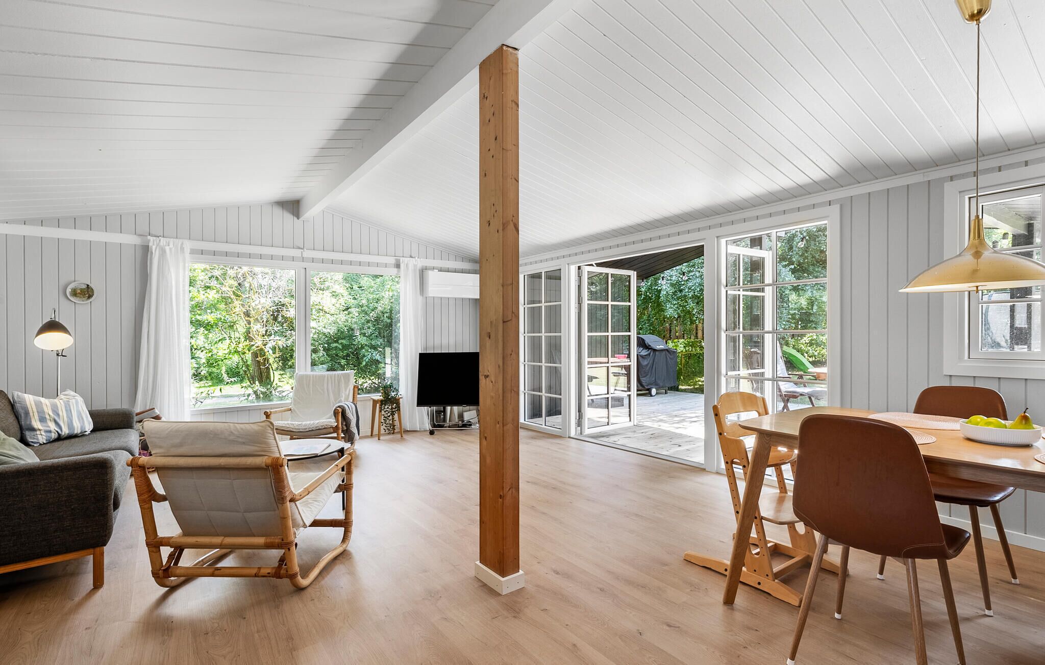 A spacious living area with a large wooden beam, a sofa, a TV, and a dining table with chairs.