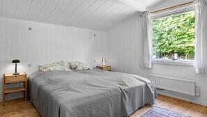 A bedroom with a large bed, wooden nightstands, a window with curtains, and a radiator.