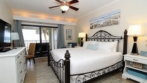 A hotel room with a bed, a desk, a chair, a TV, a ceiling fan, and a view of the outdoors. - Shipwatch A201 (Pensacola)