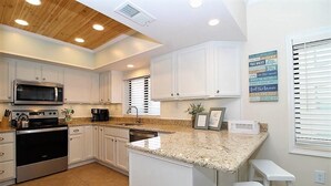 A modern kitchen with white cabinets, a granite countertop, stainless steel appliances, and a wooden ceiling. - Shipwatch A201 (Pensacola)