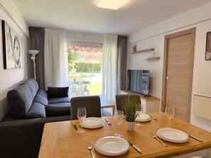 Un comedor con una mesa dispuesta para cuatro, un sofá, un televisor y una puerta al fondo.