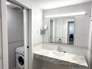 A bathroom with a washing machine, a sink with a marble countertop, and a mirror. - Cozy Apartment in Salou: Large Terrace, Pool, Near Beach & Attractions, Sleeps 6 (Salou)