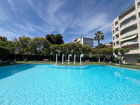 A swimming pool with clear blue water, surrounded by greenery and buildings.