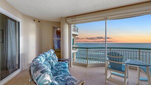 A balcony with a sofa and a chair, overlooking a sunset over the ocean. - Beach Colony West 9D (Pensacola)