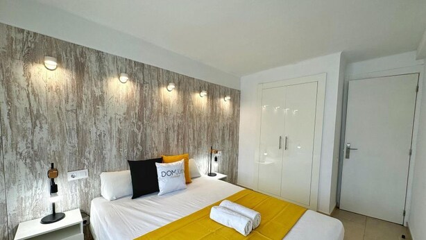 A hotel room with a bed, bedside tables, a wardrobe, and wall-mounted lights. - Cozy Apartment with Garden, Pool & Parking - Steps from Playa del Llevant! (Salou)
