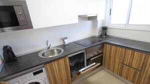 A compact kitchen with a built-in dishwasher, a coffee maker, and a microwave. - Cozy Apartment with Garden, Pool & Parking - Steps from Playa del Llevant! (Salou)
