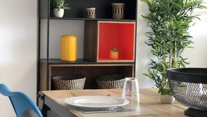 A dining area with a wooden table, chairs, and a bookshelf with various items. - Cozy Apartment with Garden, Pool & Parking - Steps from Playa del Llevant! (Salou)