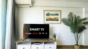 Una habitación con una televisión sobre un mueble de madera, una planta en maceta y un cuadro colgado en la pared.