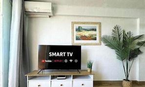 A room with a TV on a wooden stand, a potted plant, and a framed picture on the wall.