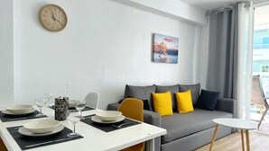 Una sala de estar moderna con comedor, un sofá con cojines amarillos, un reloj en la pared y un cuadro.