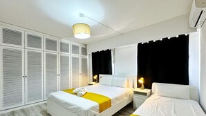 Une chambre d’hôtel avec deux lits, une armoire, un luminaire au plafond et une table de chevet avec une lampe.