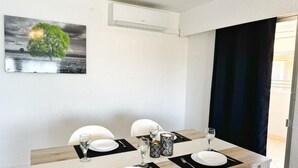 Un coin repas avec une table dressée pour deux personnes, un tableau représentant un arbre accroché au mur et un appareil de climatisation placé au-dessus de la table.
