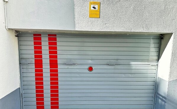 A closed garage door with red stripes and a yellow warning sign above it. - Cozy Apartment in Salou with Wi-Fi, A/C, Parking, and Terrace - 50m from Capellans Beach (Salou)