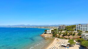 Un hôtel situé sur la côte, avec plusieurs étages, une plage au premier plan et des montagnes en arrière-plan.