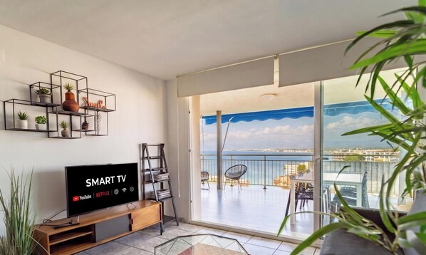 Una sala de estar moderna con un televisor de pantalla plana, un balcón con vistas al mar y un estante con plantas en la pared.