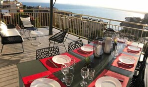 A dining table set for four with red placemats, clear glasses, and a view of the sea.
