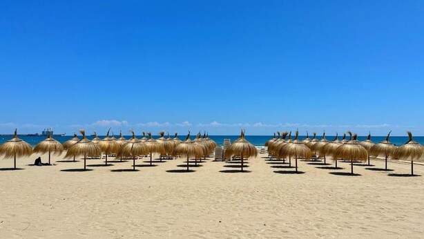 Una spiaggia con ombrelloni di paglia e un cielo azzurro limpido.