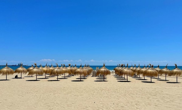 A beach with thatched umbrellas and a clear blue sky.