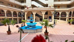 A courtyard with a central fountain, potted plants, and a multi-level building with balconies.
