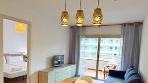 A modern hotel room with a dining area, a balcony with a view, and a television on a cabinet.