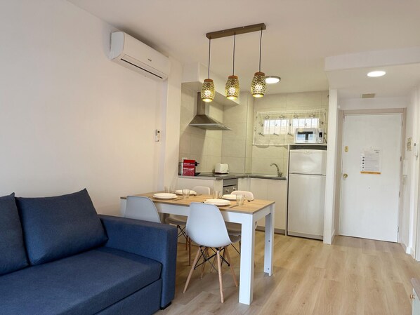 Un espace de vie compact comprenant un canapé, une table à manger, des chaises, un coin cuisine et une porte sur laquelle est affichée une note.