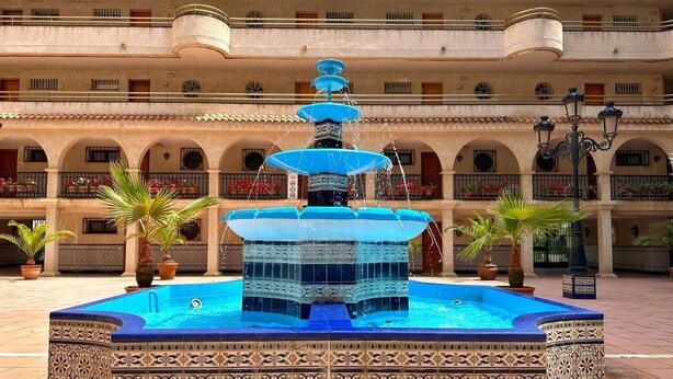 A multi-story building with a central fountain, balconies with railings, and potted plants.
