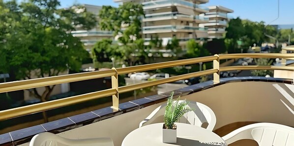 Ein Balkon mit gelber Geländer, einem Blumentopf und Blick auf umliegende Gebäude und Bäume.