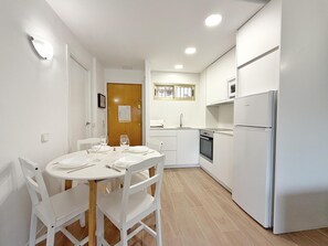 Una cocina compacta con armarios blancos, horno empotrado y refrigerador.