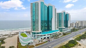 Un hôtel de grande hauteur doté de nombreux balcons, d’un espace piscine et offrant une vue sur la plage et l’océan.