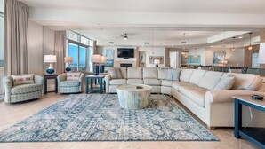 Un salon spacieux avec un grand canapé d’angle, une table basse ronde et un tapis à motifs.