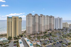 Een hoog hotel met meerdere verdiepingen, een parkeerplaats en uitzicht op het strand.