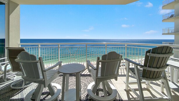 A balcony with two Adirondack chairs and a small table, overlooking a beach with clear blue water and a white railing. - Indigo West 1104 (Pensacola)