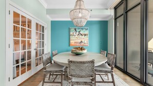 A dining area with a round table, wicker chairs, a chandelier, and a painting on the wall. - Phoenix West 1508 (Orange Beach)