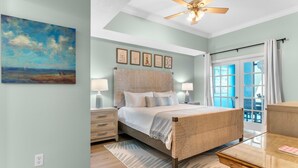 A bedroom with a large bed, bedside tables, a ceiling fan, and a view of the outdoors through a glass door. - Phoenix West 1508 (Orange Beach)