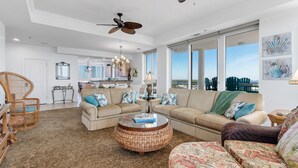 A spacious living room with a large sofa, a round coffee table, and a dining area in the background. - La Playa 801 (Pensacola)