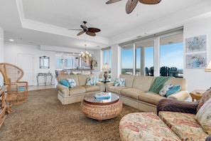A spacious living room with a large sofa, a round coffee table, and a dining area in the background. - La Playa 801 (Pensacola)