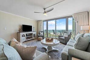 A spacious living room with a flat-screen TV, grey sofas, a coffee table, and a balcony with a view of the ocean. - Perdido Towers West 307 (Pensacola)