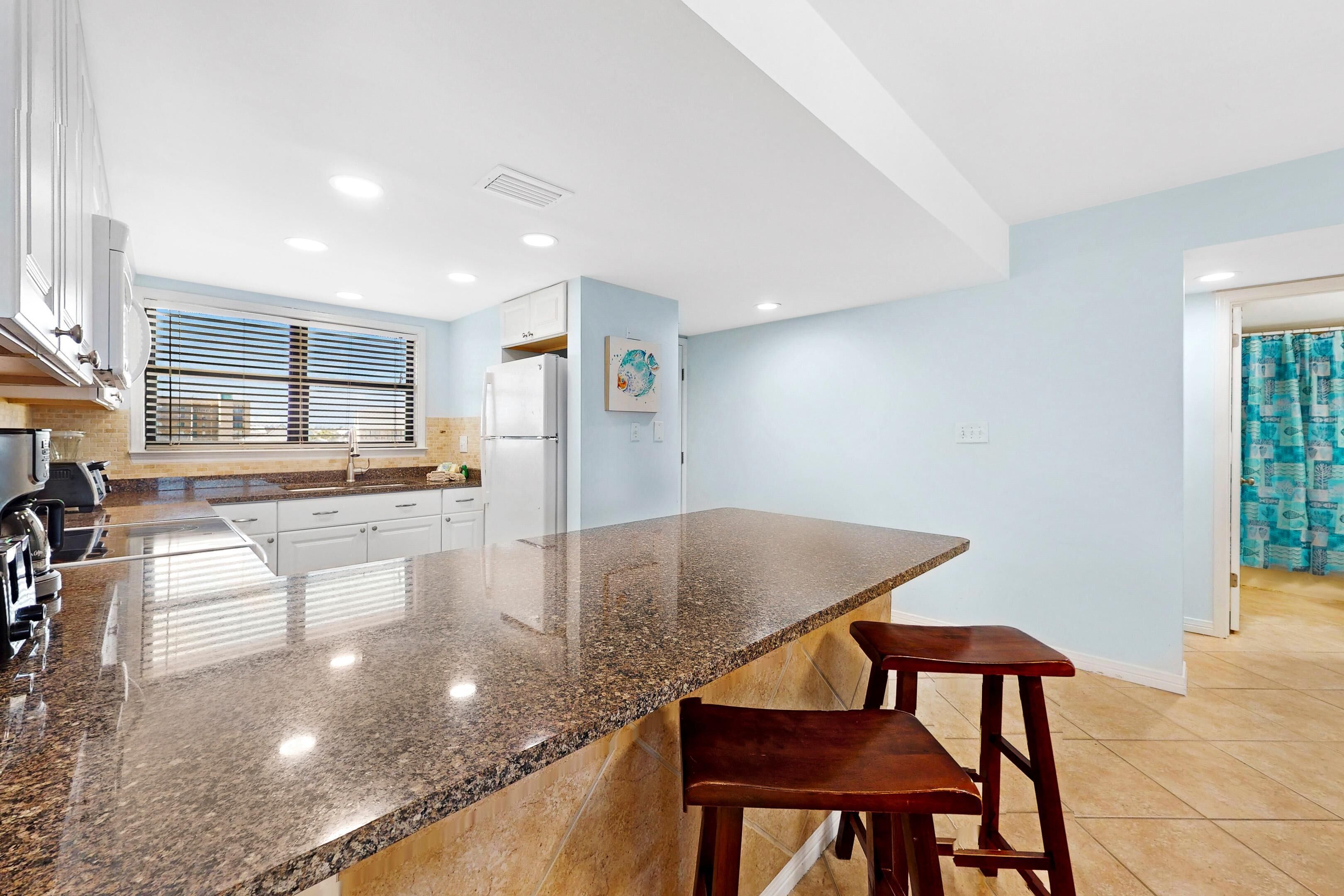 Una cocina moderna con encimera de granito, electrodomésticos de acero inoxidable y una ventana con persianas.