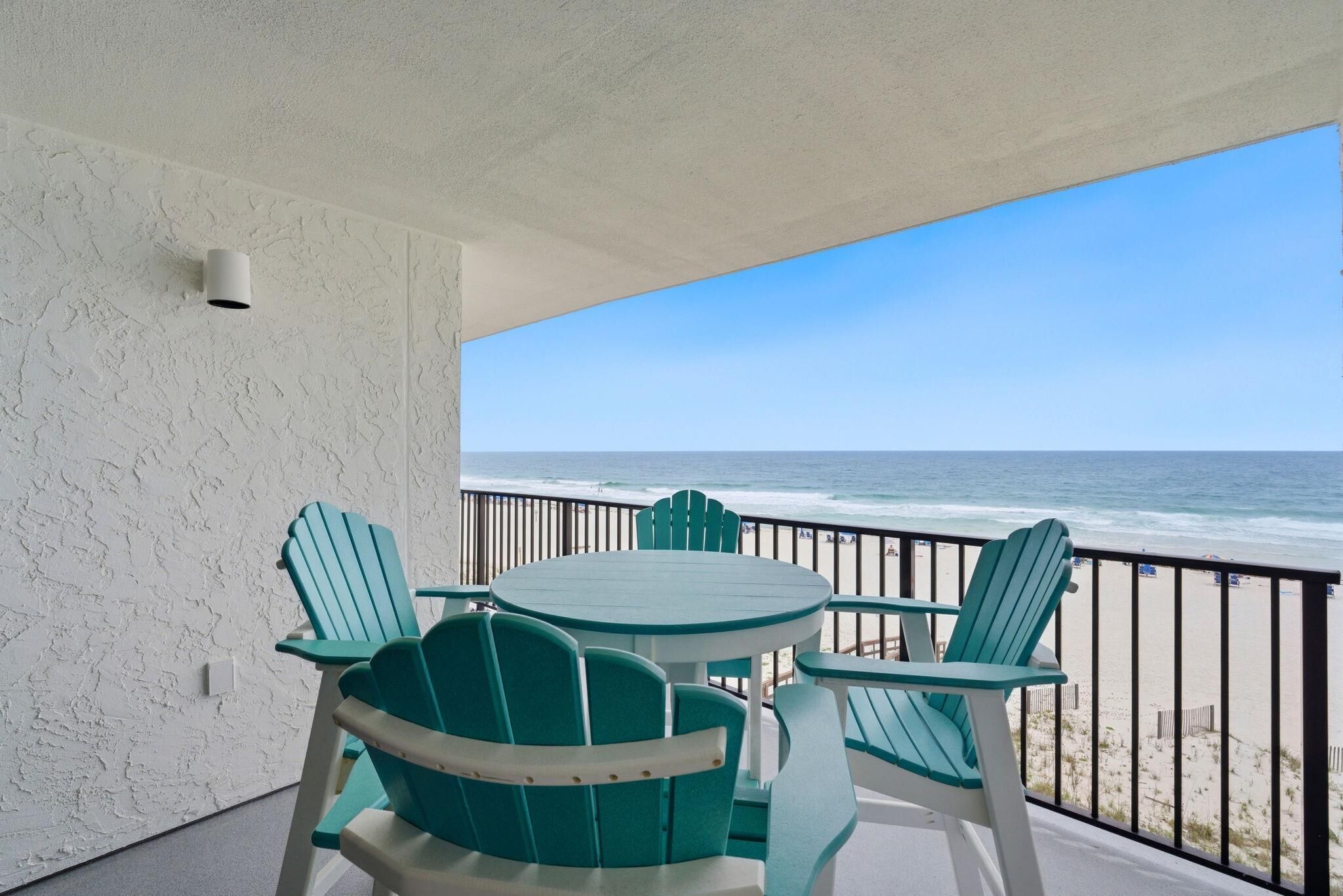 A balcony with a view of the beach, a round table, and four green chairs.