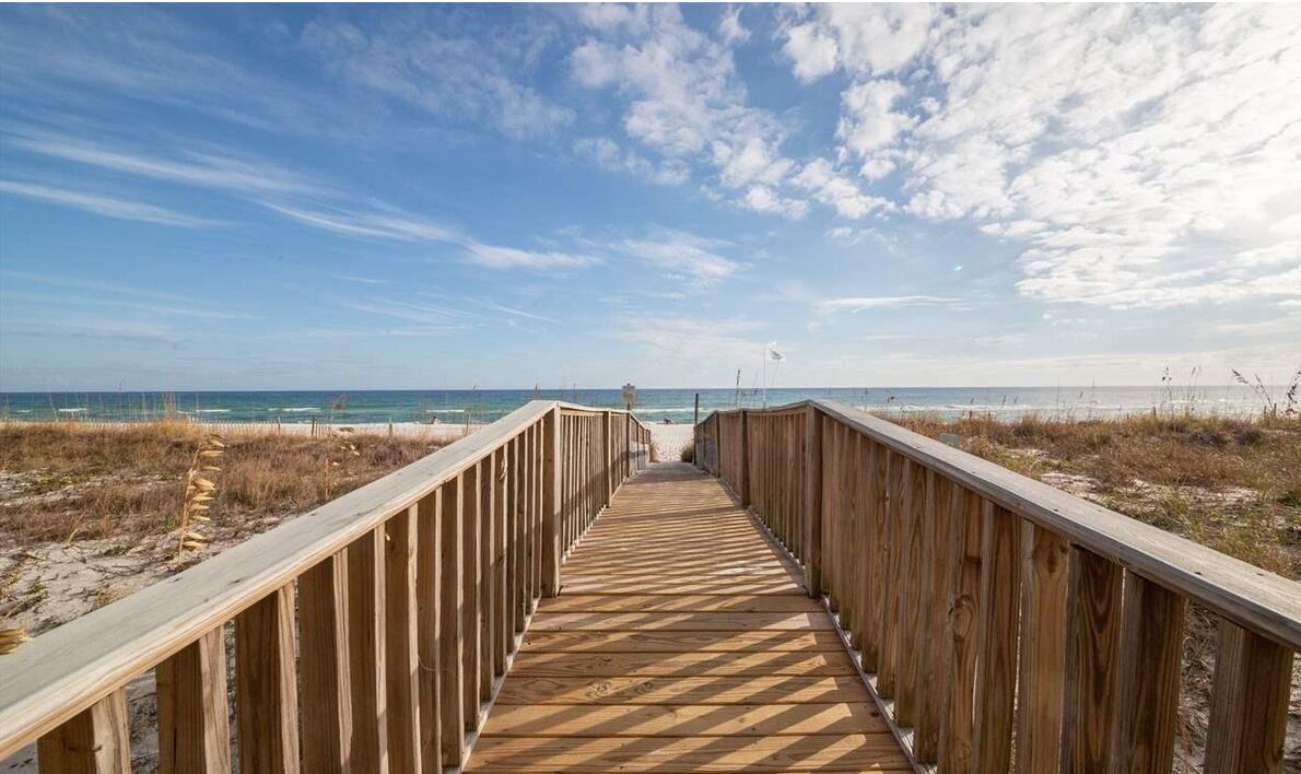 A wooden boardwalk leading to a beach with a clear sky.
