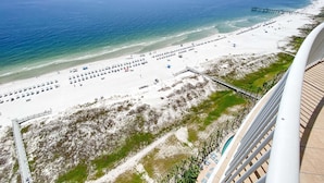A beach with rows of sun loungers and umbrellas, a pier extending into the water, and a view of the ocean. - Turquoise C1706 (Orange Beach)