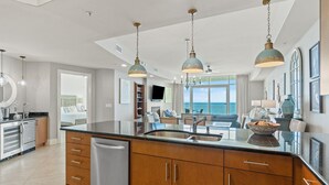 A modern kitchen with a large island, stainless steel appliances, and pendant lighting. - Turquoise C1706 (Orange Beach)
