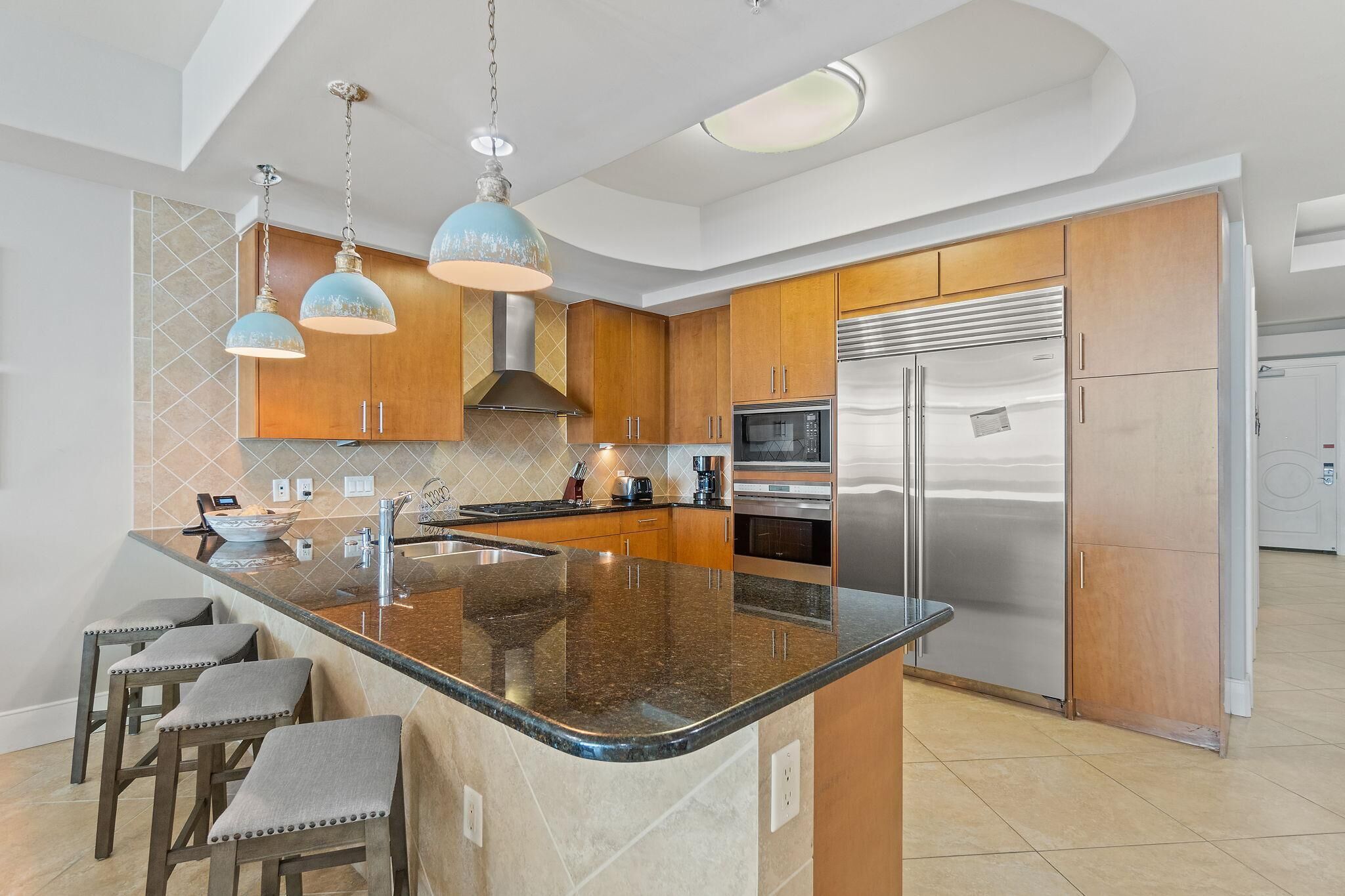 Una cucina moderna con un'ampia isola, elettrodomestici in acciaio inossidabile e illuminazione a sospensione.