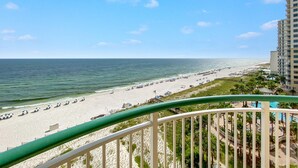A beach view from a balcony with a clear sky, a sandy beach, and a hotel building in the background. - Beach Colony West 8D (Pensacola)