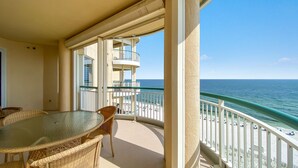 A balcony with a glass table and wicker chairs, overlooking a beach with a clear view of the ocean and a white fence. - Beach Colony West 8D (Pensacola)
