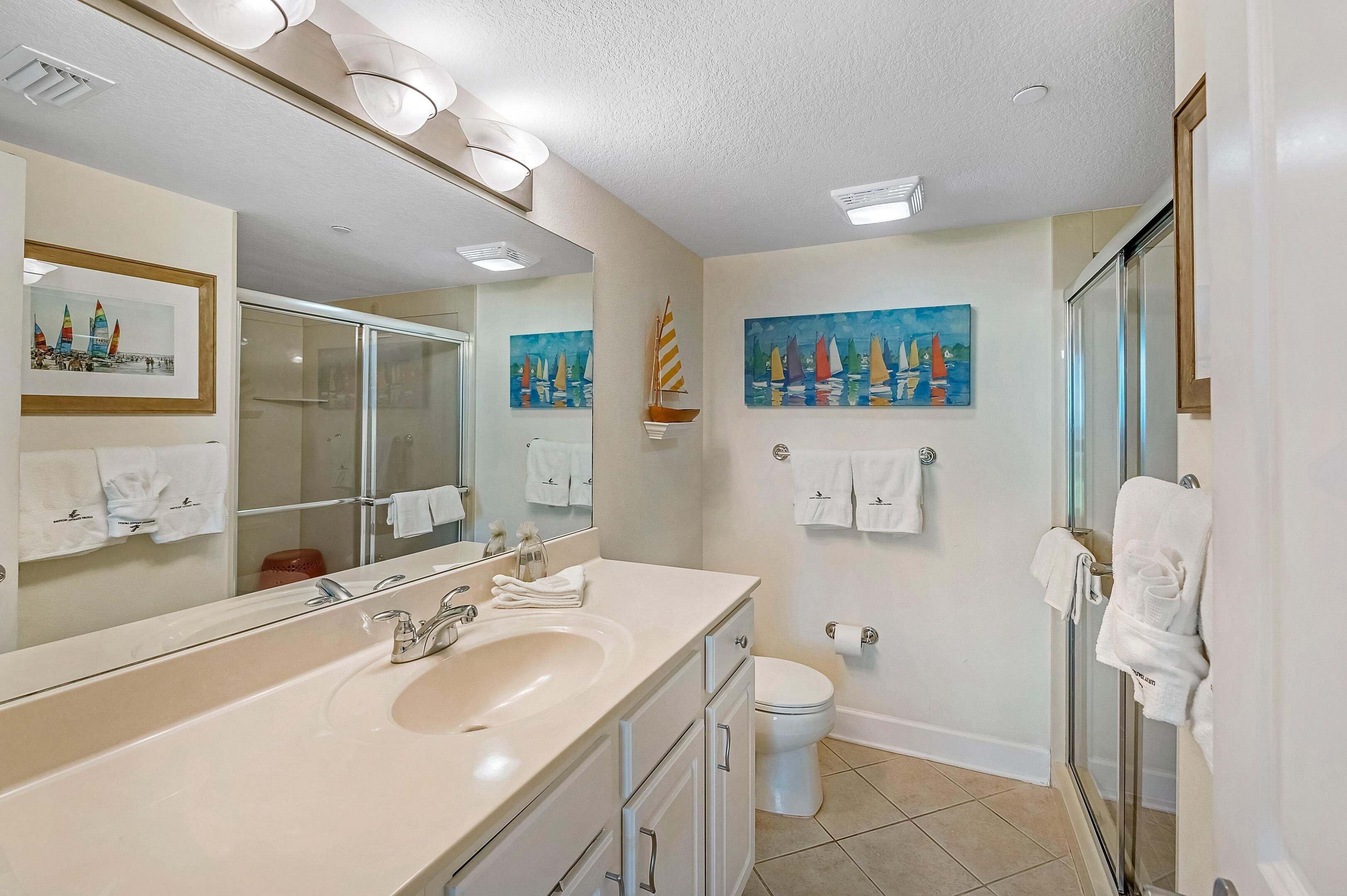 Une salle de bain moderne avec un grand miroir, un lavabo, des toilettes et une douche à parois de verre.