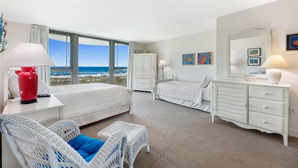 Ein Hotelzimmer mit einem großen Bett, einem kleineren Bett, einem Schminktisch, einem Sessel und Blick aufs Meer.