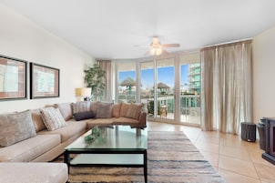 A spacious living room with a large sofa, a glass coffee table, and a balcony with a view of the city.
