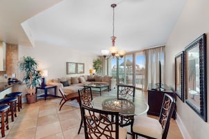 A spacious living area with a round glass table, comfortable seating, and large windows offering a view.