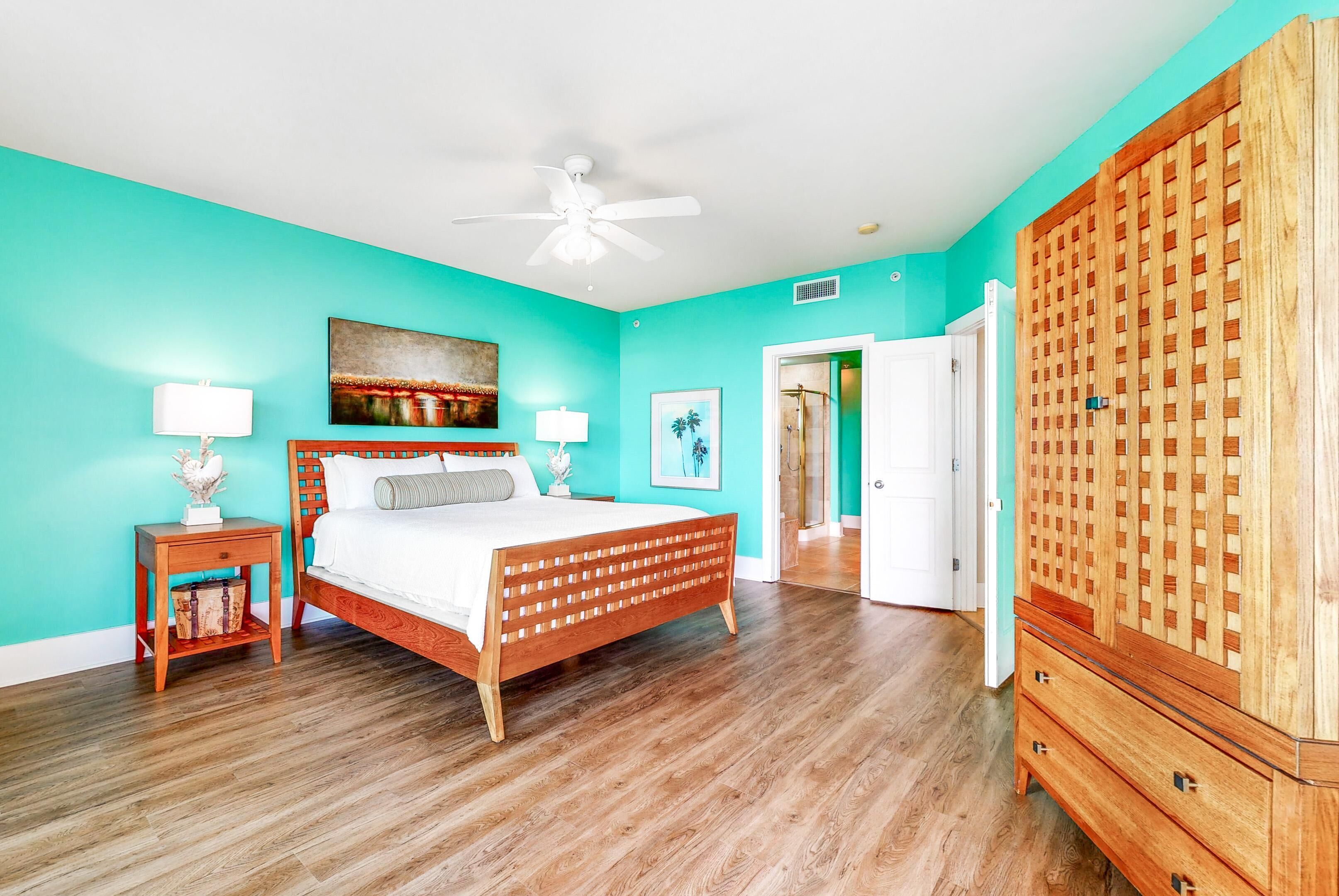 A bedroom with a wooden bed, a ceiling fan, a teal wall, and a wooden wardrobe.